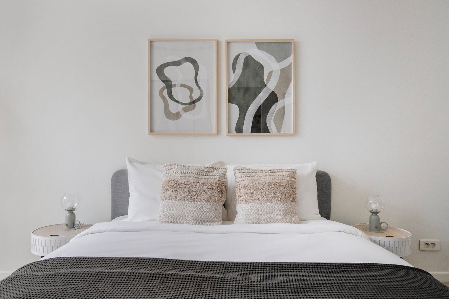 A bedroom with a bed, two pillows, two bedside tables, and two abstract paintings on the wall.