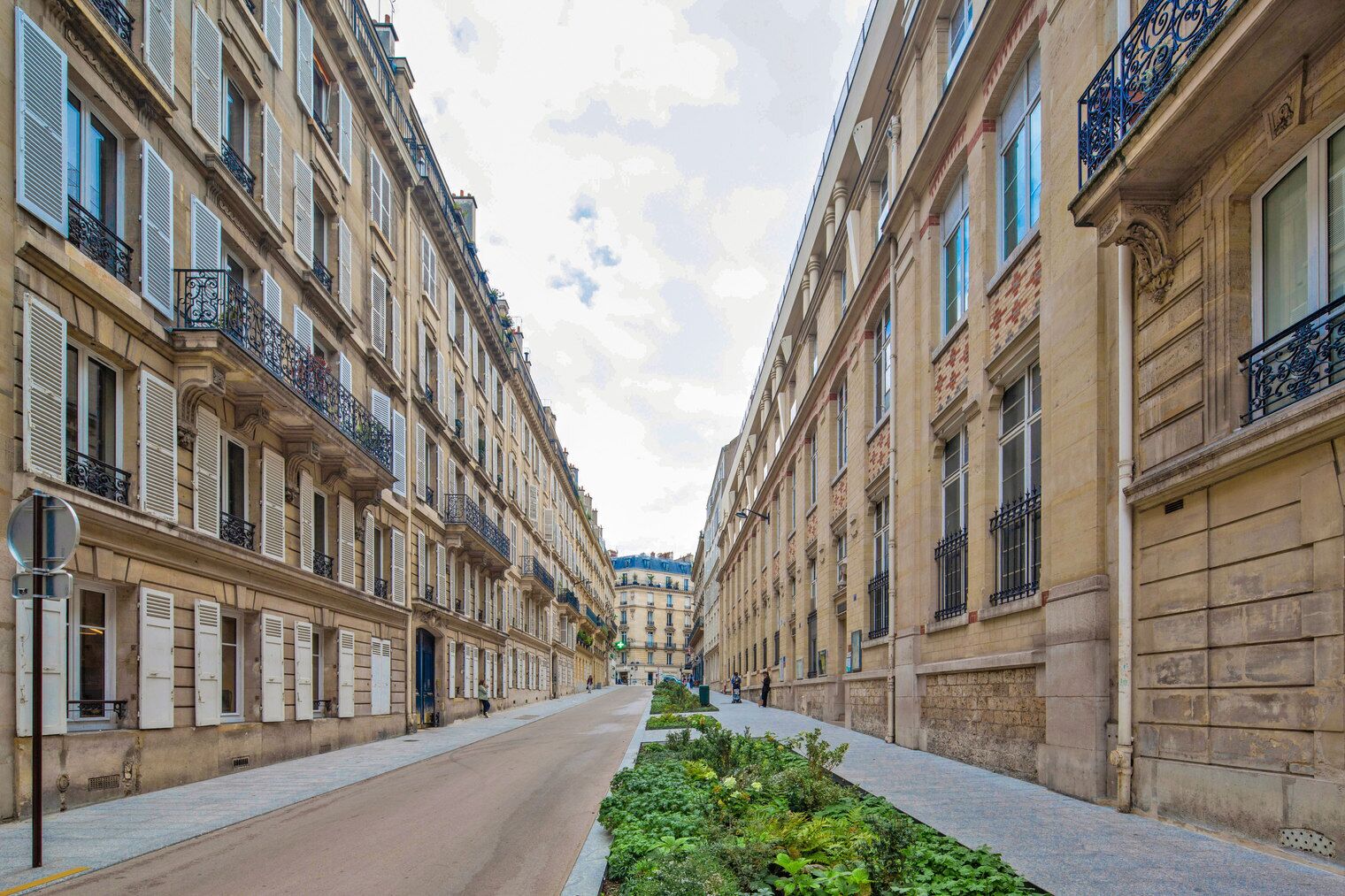 A narrow street flanked by historic buildings with balconies and shutters.