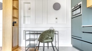 A modern kitchen with a built-in oven, a wooden cabinet, and a green upholstered chair. - Blueground | Rochechouart, furnished, balcony (Paris)