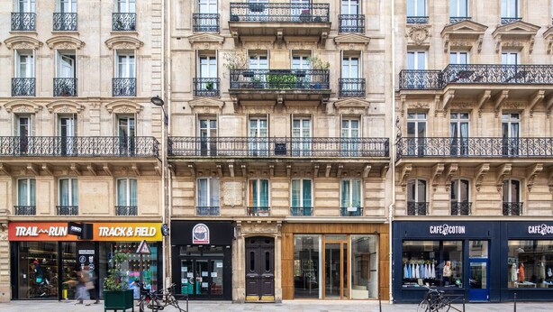 A row of buildings with storefronts including a track and field store, a cafe, and a clothing store. - Blueground | Bourse Sentier/Les Halles, nr Louvre (Paris)