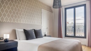 A neatly arranged bedroom with a large bed, a bedside table with a lamp, a window with a view of buildings, and patterned wallpaper. - Blueground | Bourse Sentier/Les Halles, nr Louvre (Paris)