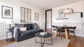 A modern living room with a grey sofa, a round coffee table, and a dining area with a table and chairs. - Blueground | Bourse Sentier/Les Halles, nr Louvre (Paris)