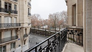 Vista de uma varanda com vista para uma rua repleta de cerejeiras, um rio e uma ponte.