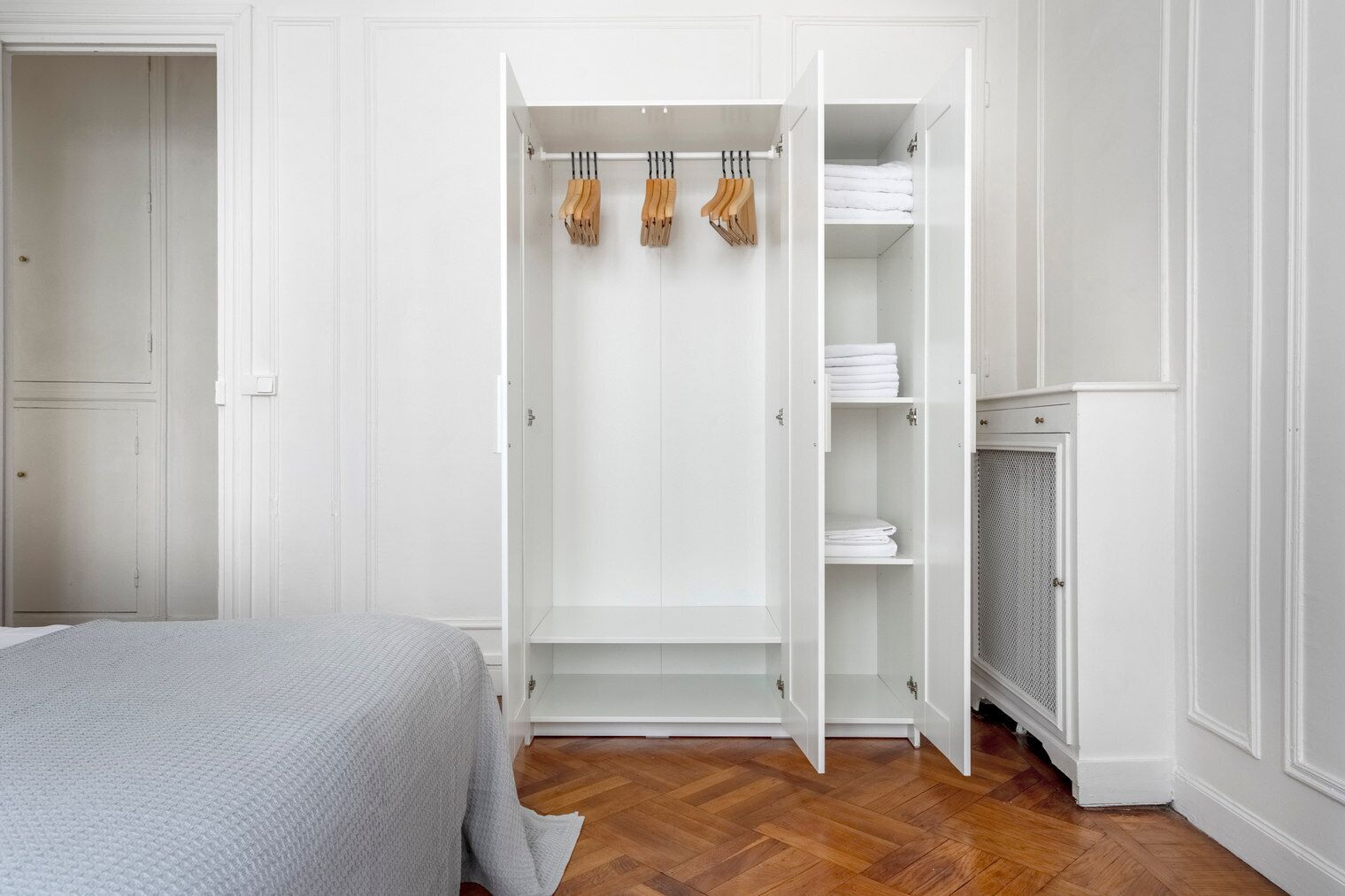 A bedroom with a bed, a white wardrobe with hanging space, and a radiator.