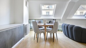 A modern loft apartment with a dining area, a sofa, and a large window providing natural light.