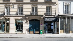 A street view with a building featuring a storefront labeled "Oscar Fabricat" and another labeled "Immobiliers."