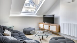 A modern loft apartment with a skylight, a flat-screen TV, a glass coffee table, and a sofa.