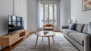 Un salon moderne avec un téléviseur à écran plat, une table basse ronde, un canapé et un fauteuil.