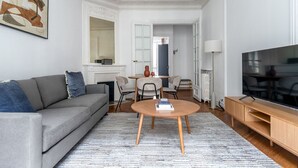 Un salon moderne avec un canapé gris, une table basse ronde en bois et un téléviseur à écran plat posé sur un meuble en bois.