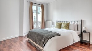 A bedroom with a bed, a nightstand, a window with curtains, and a radiator. - Blueground | Lamark-Caulaincourt, elevator (Paris)