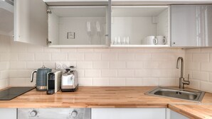 A modern kitchen with white brick backsplash, stainless steel appliances, and a wooden countertop. - Blueground | Lamark-Caulaincourt, elevator (Paris)