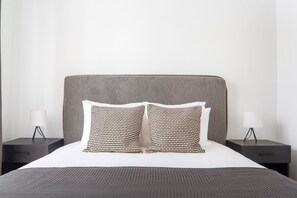A bed with a grey headboard, two patterned pillows, and a grey blanket. There are two bedside tables with lamps on either side of the bed. - Blueground | Miromesnil, elev, nr Champs Elysées (Paris)