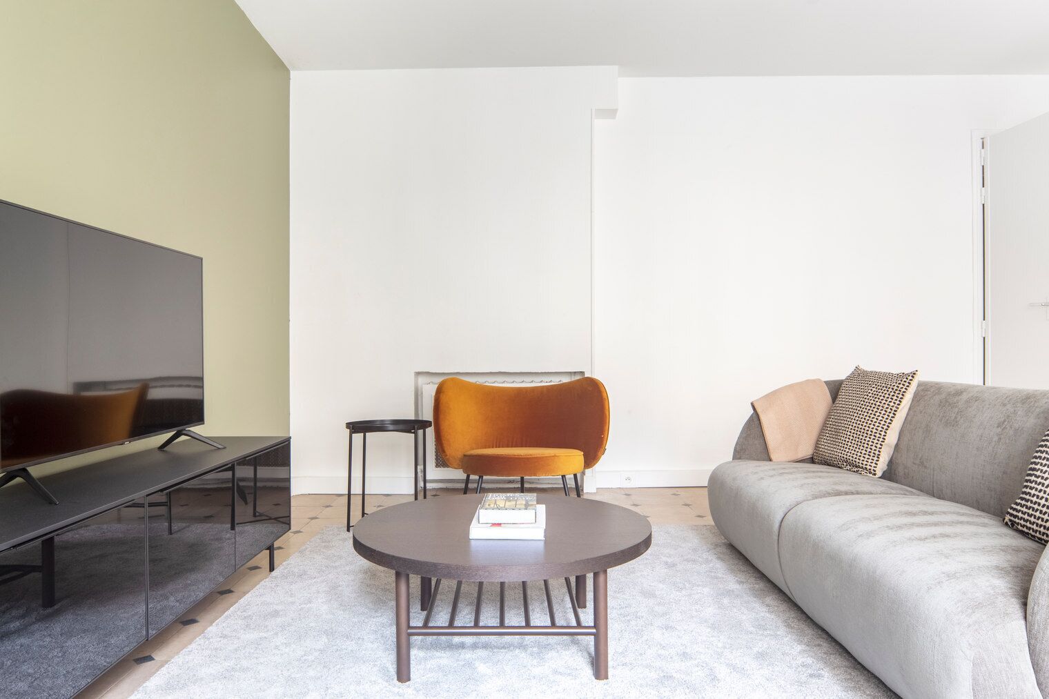 En moderne stue med et fladskærms-TV, et rundt sofabord, en sofa og en stærk orange lænestol.
