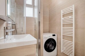 A modern bathroom with a white sink, a glass shower enclosure, and a front-loading washing machine.