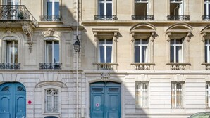 A building with multiple windows, a blue door, and a black car parked in front. - Blueground | Invalides, balcony & elev nr gardens (Paris)