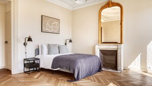 A bedroom with a bed, two bedside lamps, a fireplace, and a large mirror. - Blueground | Invalides, balcony & elev nr gardens (Paris)