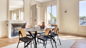 A dining room with a fireplace, large windows, and a view of the city. - Blueground | Invalides, balcony & elev nr gardens (Paris)