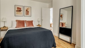 A bedroom with a large bed, two bedside tables with lamps, a large mirror, and abstract artwork on the wall. - Blueground | Jules-Joffrin, furnished & equipped (Paris)