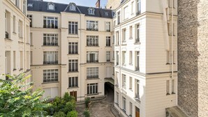 A multi-story building with a courtyard, featuring balconies and a stone wall. - Blueground | Neuilly, nr dining, gardens & shops (Paris)