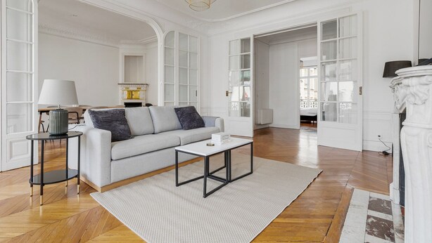 A spacious living room with a sofa, coffee table, and lamp. There are open doors leading to other rooms. - Blueground | Neuilly, nr dining, gardens & shops (Paris)
