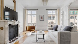 A spacious living room with a fireplace, a sofa, a coffee table, and a TV. - Blueground | Neuilly, nr dining, gardens & shops (Paris)