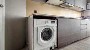 A compact kitchen with a built-in washer and dryer, wooden cabinets, and a light-colored backsplash. - Blueground | Canal Saint Martin, near shops (Paris)