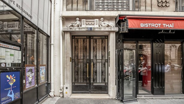 A building facade with a black metal gate, a red awning with "BISTROT THAI" signage, and a stone plaque above the entrance. - Blueground | Canal Saint Martin, near shops (Paris)