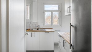 Et moderne køkken med hvide skabe, et rustfrit stål køleskab, et vindue med udsigt og en træbordplade.