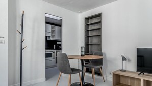 Ein modernes Wohnzimmer mit Esstisch, zwei Stühlen, Fernseher, Bücherregal und Garderobe.