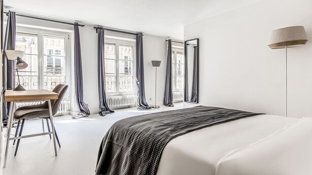 Ein Hotelzimmer mit einem Bett, einem Schreibtisch mit Stuhl und großen Fenstern mit Vorhängen.