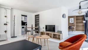Ein modernes Wohnzimmer mit einer schwarzen Couch, zwei Holztischen, einem roten Sessel, einem Fernseher und einem Bücherregal.