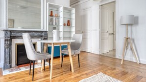 A room with a fireplace, a round table with chairs, a glass shelving unit, and a lamp.