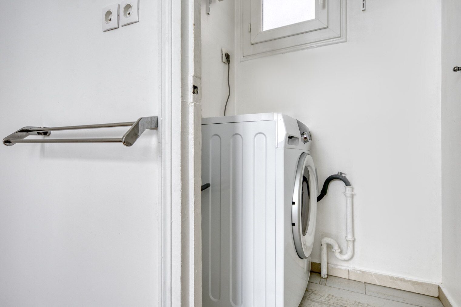A laundry room with a front-loading washing machine, a towel rack, and a door with a handle.