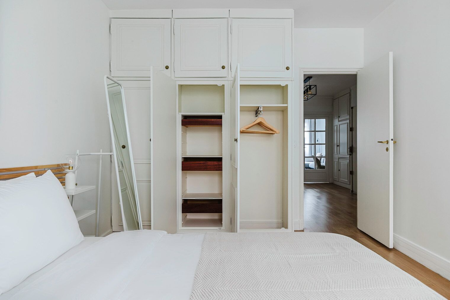 Een slaapkamer met een bed, een openstaande garderobe, een nachtkastje en een hanglamp.
