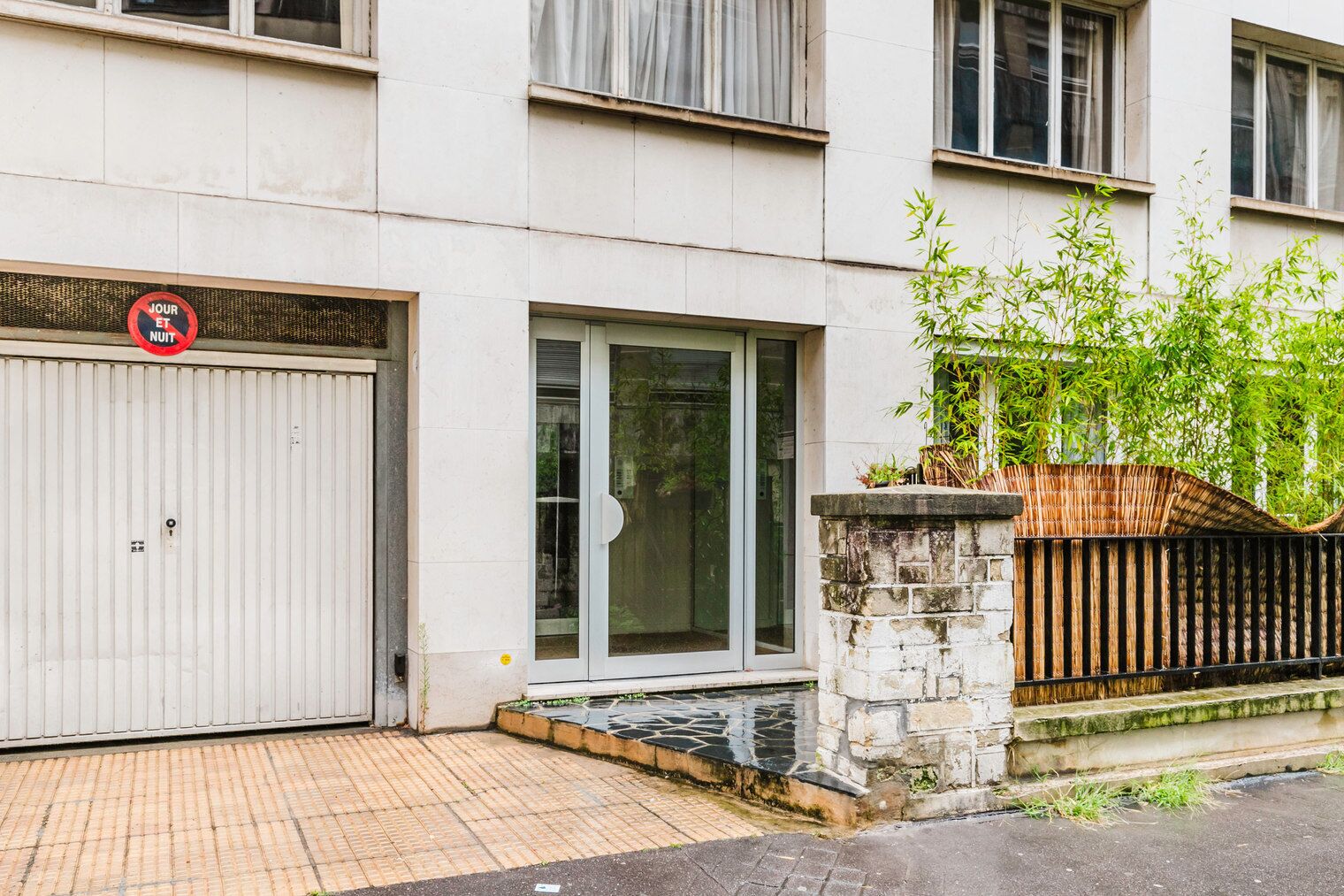 A building with a closed garage door, a glass door entrance, and a bamboo fence.