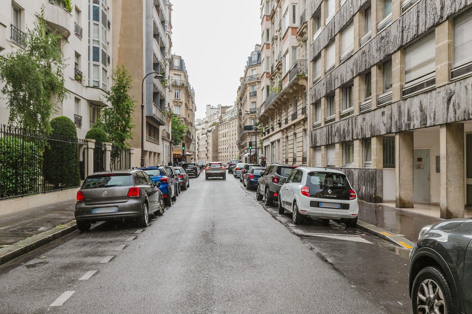 Een straat met geparkeerde auto's en meerlaags gebouwen met balkons.