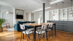 A modern living room with a wooden dining table, grey and teal sofas, and a TV. - Blueground | Saint Georges, nr Palais Garnier (Paris)