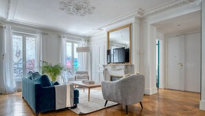 A spacious living room with a blue sofa, a grey armchair, and a wooden herringbone floor. - Blueground | Saint Georges, nr Palais Garnier (Paris)