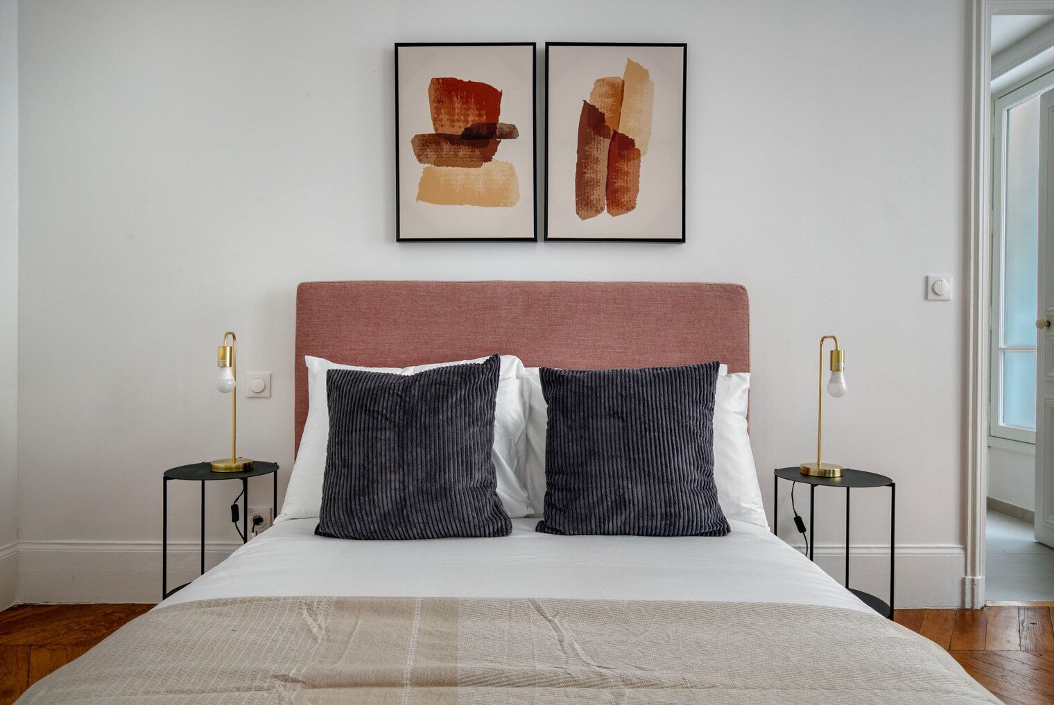 A bedroom with a bed, two bedside tables, two lamps, and two framed artworks on the wall.