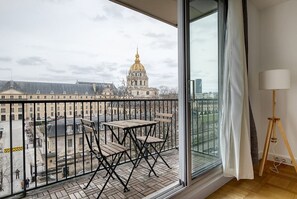 A balcony with a view of a historic building with a golden dome, a wooden table and chairs, and a floor lamp. - Blueground | Invalides, balcony, nr embassies (Paris)