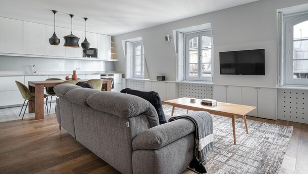 Ein stilvoller Wohnraum mit grauem Sofa, einem Holzesstisch und einem an der Wand montierten Fernseher.