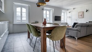 Ein großzügiger Wohnbereich mit einem Holzessttisch, grünen und beigen Stühlen, einem grauen Sofa und einem Fernseher an der Wand.