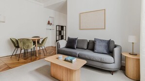 A modern living room with a grey sofa, a wooden coffee table, and a dining area with a green chair and a small table. - Blueground | Pigalle, washer, nr festive area (Paris)