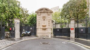 A gated entrance with a stone monument, a paved road, and a parked motorcycle. - Blueground | Pigalle, washer, nr festive area (Paris)
