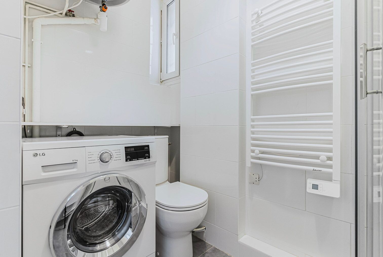 A compact laundry room with a front-loading LG washer and dryer, a white toilet, and a built-in towel rack.