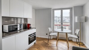 Une cuisine compacte avec des meubles blancs, un four à micro-ondes, une machine à café et un coin repas comprenant une table ronde et deux chaises.