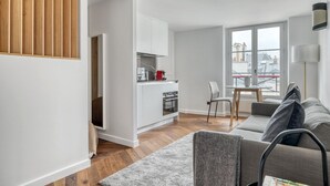 Un espace de vie compact comprenant un coin cuisine, un coin repas et un coin salon avec un canapé et un fauteuil.