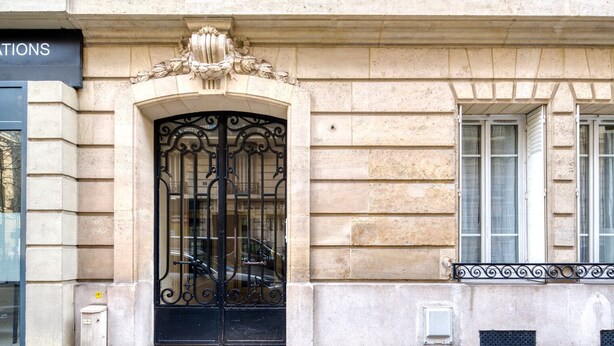 Une façade d’immeuble ornée d’un grand portail en fer forgé noir, d’un mur en pierre et d’une fenêtre avec des volets.