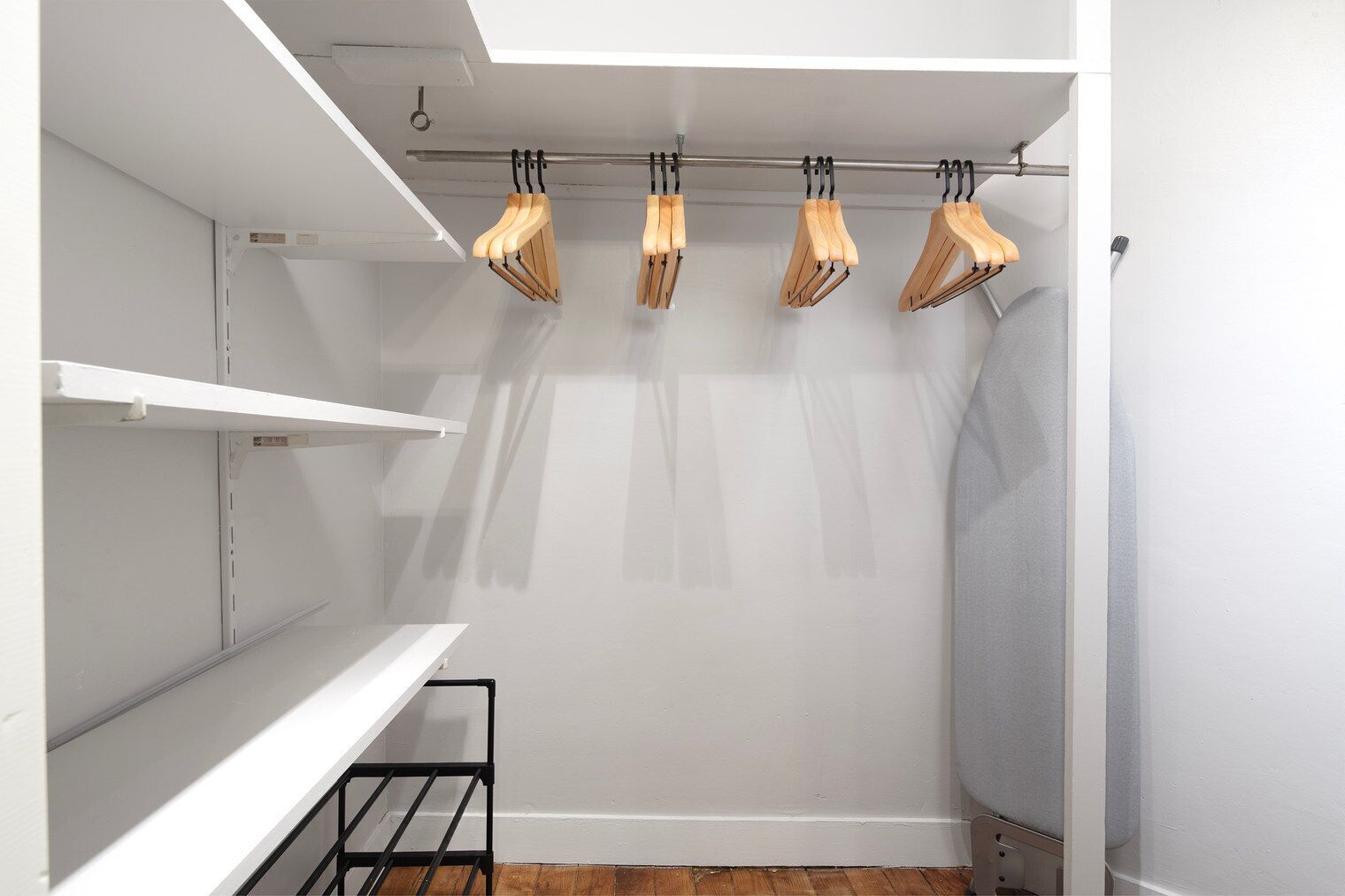 Un dressing avec des murs blancs, des cintres en bois et des étagères en métal.