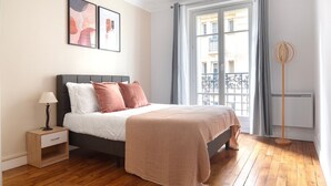 Une chambre à coucher avec un lit, une table de chevet, une lampe et une fenêtre avec des rideaux.